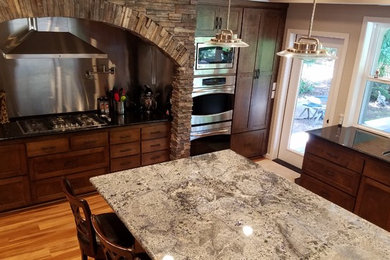 Example of a large classic u-shaped medium tone wood floor and brown floor kitchen design in Other with an undermount sink, shaker cabinets, dark wood cabinets, granite countertops, metal backsplash, stainless steel appliances, an island and black countertops