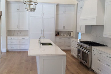 Design ideas for a large transitional u-shaped eat-in kitchen in Miami with an undermount sink, recessed-panel cabinets, white cabinets, marble benchtops, white splashback, stone slab splashback, panelled appliances, light hardwood floors, with island, beige floor and white benchtop.