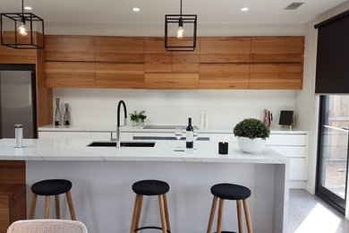 Inspiration for a mid-sized contemporary galley open plan kitchen in Melbourne with an undermount sink, recessed-panel cabinets, medium wood cabinets, quartz benchtops, white splashback, porcelain splashback, stainless steel appliances, concrete floors, with island and grey floor.
