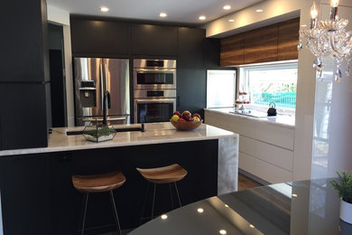Example of a mid-sized trendy u-shaped medium tone wood floor and brown floor eat-in kitchen design in Montreal with an undermount sink, flat-panel cabinets, black cabinets, quartzite countertops, stainless steel appliances, a peninsula and white countertops