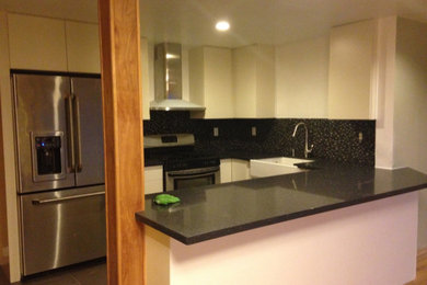Small trendy galley ceramic tile and gray floor eat-in kitchen photo in Seattle with a farmhouse sink, flat-panel cabinets, white cabinets, quartz countertops, black backsplash, glass tile backsplash, stainless steel appliances, a peninsula and black countertops