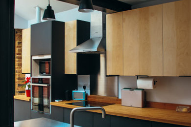 Ejemplo de cocina urbana abierta con armarios con paneles lisos, puertas de armario negras, encimera de madera, suelo de cemento, una isla, suelo gris y vigas vistas