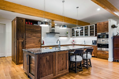 Open concept kitchen - large transitional l-shaped medium tone wood floor and brown floor open concept kitchen idea in Other with an undermount sink, shaker cabinets, dark wood cabinets, granite countertops, white backsplash, glass tile backsplash, stainless steel appliances and an island