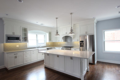 Eat-in kitchen - mid-sized transitional l-shaped brown floor and dark wood floor eat-in kitchen idea in Other with recessed-panel cabinets, white cabinets, quartzite countertops, an island, a farmhouse sink, gray backsplash, ceramic backsplash and stainless steel appliances
