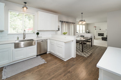 Example of a farmhouse medium tone wood floor and brown floor kitchen design in Detroit with a farmhouse sink, white cabinets, quartz countertops, white backsplash, ceramic backsplash, stainless steel appliances and white countertops