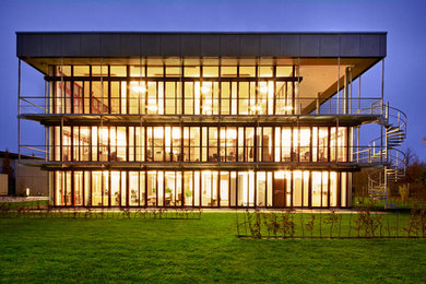 Modelo de fachada gris actual grande de tres plantas con revestimiento de vidrio y tejado plano