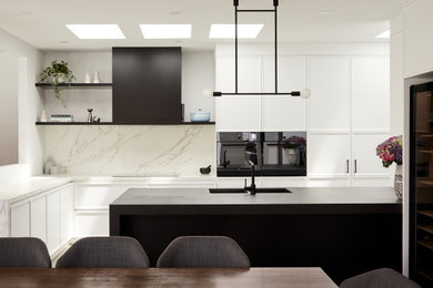 This is an example of a mid-sized modern galley open plan kitchen in Melbourne with an undermount sink, shaker cabinets, white cabinets, solid surface benchtops, white splashback, stone slab splashback, black appliances, a peninsula and grey benchtop.