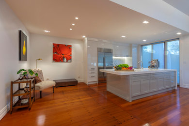 Inspiration for a mid-sized transitional single-wall eat-in kitchen in Auckland with an undermount sink, recessed-panel cabinets, white cabinets, solid surface benchtops, grey splashback, marble splashback, stainless steel appliances, medium hardwood floors, with island, brown floor and white benchtop.