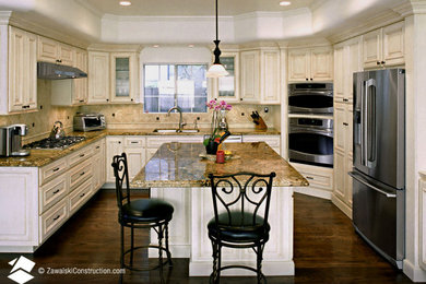 Example of a classic dark wood floor and brown floor kitchen design in Los Angeles with raised-panel cabinets, white cabinets, travertine backsplash, stainless steel appliances and beige countertops