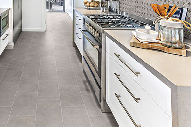 Mid-sized trendy galley porcelain tile and gray floor enclosed kitchen photo in Orange County with a farmhouse sink, flat-panel cabinets, white cabinets, quartz countertops, multicolored backsplash, stone tile backsplash, stainless steel appliances, no island and gray countertops