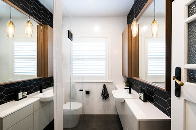 Mid-sized contemporary master bathroom in Melbourne with furniture-like cabinets, white cabinets, a corner shower, a two-piece toilet, black tile, subway tile, white walls, porcelain floors, a drop-in sink, engineered quartz benchtops, grey floor, a hinged shower door and white benchtops.