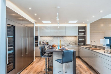 Inspiration for a large modern u-shaped medium tone wood floor and brown floor enclosed kitchen remodel in Hawaii with an undermount sink, flat-panel cabinets, white cabinets, solid surface countertops, gray backsplash, marble backsplash, black appliances, an island and gray countertops