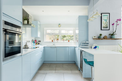 This is an example of a medium sized nautical u-shaped open plan kitchen in Dorset with a submerged sink, flat-panel cabinets, blue cabinets, white splashback, integrated appliances, terracotta flooring, no island, brown floors and white worktops.