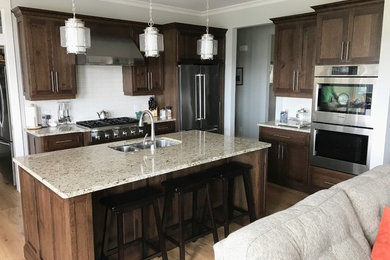 This is an example of an arts and crafts kitchen in Other with an undermount sink, shaker cabinets, brown cabinets, white splashback, subway tile splashback, stainless steel appliances, light hardwood floors and brown floor.