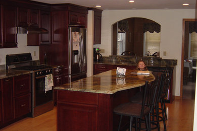 Inspiration for a mid-sized contemporary l-shaped light wood floor and yellow floor kitchen remodel in Other with an undermount sink, raised-panel cabinets, dark wood cabinets, granite countertops, brown backsplash, granite backsplash, stainless steel appliances, an island and brown countertops