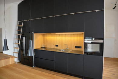 Design ideas for a large contemporary galley kitchen in Munich with a single-bowl sink, glass-front cabinets, wood benchtops, brown splashback, timber splashback, black appliances, medium hardwood floors, with island, brown floor, brown benchtop and black cabinets.