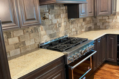 Example of a large tuscan light wood floor and brown floor enclosed kitchen design in Chicago with an undermount sink, raised-panel cabinets, dark wood cabinets, quartz countertops, beige backsplash, porcelain backsplash, black appliances, an island and beige countertops