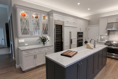 Inspiration for a mid-sized transitional u-shaped open plan kitchen in San Francisco with an undermount sink, shaker cabinets, white cabinets, quartzite benchtops, grey splashback, glass tile splashback, stainless steel appliances, light hardwood floors, with island, brown floor and grey benchtop.