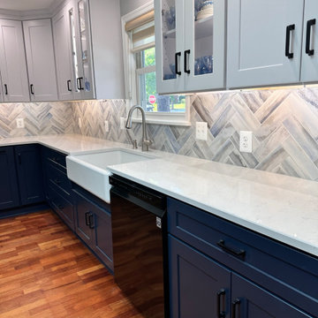 White upper cabinets with blue base cabinets with herringbone tile backsplash