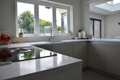 Photo of a mid-sized modern u-shaped eat-in kitchen in Essex with an undermount sink, flat-panel cabinets, beige cabinets, quartzite benchtops, white splashback, black appliances and no island.