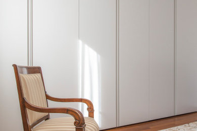 Diseño de armario unisex moderno de tamaño medio con armarios con paneles lisos, puertas de armario blancas, suelo de madera pintada y suelo marrón