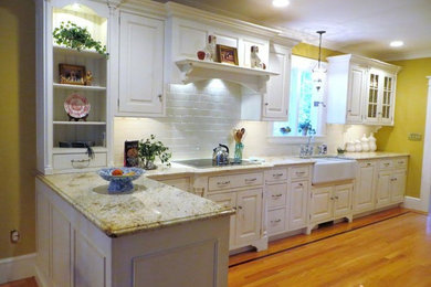 Photo of a mid-sized traditional l-shaped open plan kitchen in New York with a farmhouse sink, raised-panel cabinets, white cabinets, granite benchtops, white splashback, subway tile splashback, white appliances, medium hardwood floors and a peninsula.