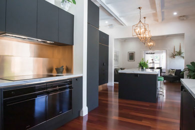 Design ideas for a large contemporary u-shaped open plan kitchen in Adelaide with an undermount sink, recessed-panel cabinets, black cabinets, quartz benchtops, metallic splashback, black appliances, medium hardwood floors, with island, white benchtop and coffered.