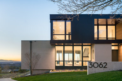 Example of a large trendy black two-story stucco flat roof design in Seattle