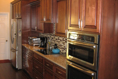 Inspiration for a large traditional galley kitchen in Tampa with dark hardwood floors, brown floor, an undermount sink, raised-panel cabinets, medium wood cabinets, granite benchtops, multi-coloured splashback, glass tile splashback, stainless steel appliances and with island.