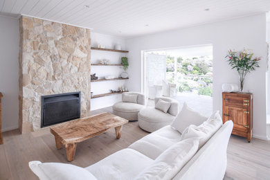 Inspiration for a mid-sized beach style open concept living room in Sydney with white walls, light hardwood floors, a wood stove, a stone fireplace surround and a wall-mounted tv.