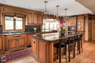 Design ideas for a traditional kitchen in Chicago with raised-panel cabinets, medium wood cabinets, black splashback, panelled appliances, medium hardwood floors, with island and brown floor.