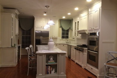 Example of a mid-sized trendy u-shaped medium tone wood floor eat-in kitchen design in DC Metro with an undermount sink, raised-panel cabinets, white cabinets, quartzite countertops, white backsplash, ceramic backsplash, stainless steel appliances and an island