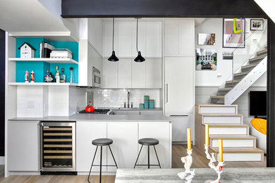 Photo of a contemporary u-shaped kitchen in New York with a drop-in sink, flat-panel cabinets, grey cabinets, white splashback, subway tile splashback, stainless steel appliances, light hardwood floors and a peninsula.