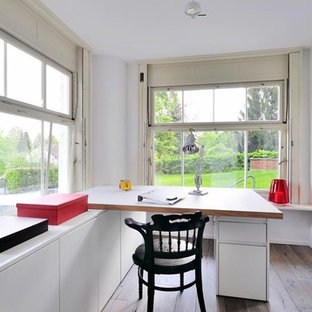 Inspiration for a large modern study in Munich with white walls, medium hardwood flooring, a built-in desk, no fireplace, a plastered fireplace surround and brown floors.