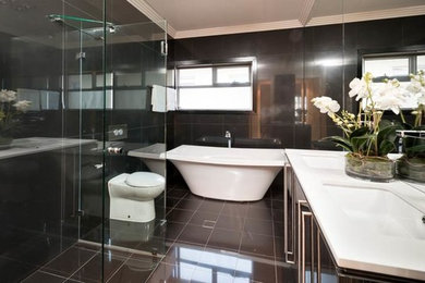 This is an example of a mid-sized contemporary bathroom in Adelaide with flat-panel cabinets, black cabinets, engineered quartz benchtops, a freestanding tub, a corner shower, black tile, porcelain tile, black walls and porcelain floors.