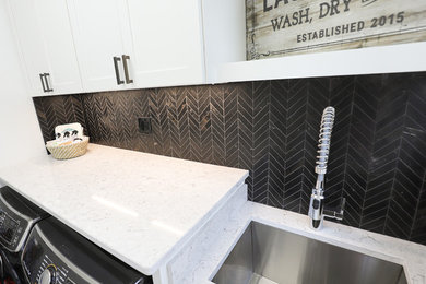 Example of a small galley ceramic tile and black floor dedicated laundry room design in Other with an undermount sink, shaker cabinets, white cabinets, quartz countertops, white walls and a side-by-side washer/dryer