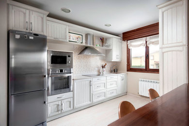 Modelo de cocina comedor lineal clásica de tamaño medio sin isla con fregadero de un seno, armarios con paneles con relieve, puertas de armario blancas, electrodomésticos de acero inoxidable y suelo de madera pintada