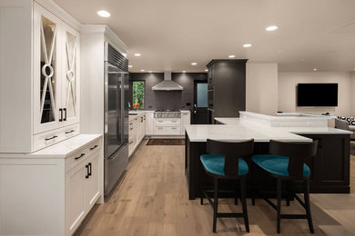 Photo of a mid-sized transitional l-shaped eat-in kitchen in Seattle with an undermount sink, beaded inset cabinets, white cabinets, black splashback, stainless steel appliances, light hardwood floors, a peninsula, brown floor and white benchtop.