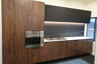 Photo of a mid-sized modern single-wall kitchen pantry in Christchurch with flat-panel cabinets, dark wood cabinets, quartz benchtops, black splashback, porcelain splashback, stainless steel appliances, carpet, no island, black floor and white benchtop.