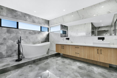 Large modern master bathroom in Brisbane with furniture-like cabinets, light wood cabinets, a freestanding tub, a shower/bathtub combo, a one-piece toilet, gray tile, ceramic tile, white walls, ceramic floors, an integrated sink, laminate benchtops, grey floor, an open shower, white benchtops, a double vanity, a built-in vanity, vaulted and panelled walls.