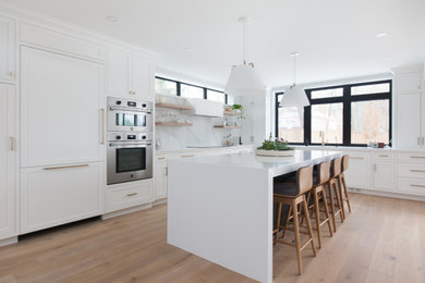 This is an example of a contemporary l-shaped kitchen in Toronto with shaker cabinets, white cabinets, medium hardwood floors, with island, brown floor and white benchtop.