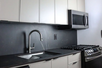 Eat-in kitchen - mid-sized modern single-wall concrete floor, gray floor and exposed beam eat-in kitchen idea in Toronto with an undermount sink, flat-panel cabinets, gray cabinets, quartz countertops, black backsplash, quartz backsplash, stainless steel appliances, an island and black countertops