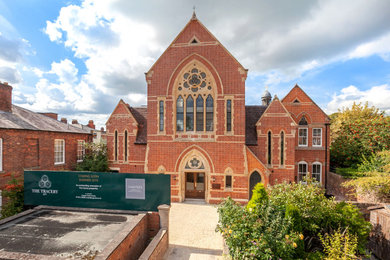This is an example of a large and red contemporary brick and front flat in West Midlands with three floors, a pitched roof, a tiled roof and a black roof.