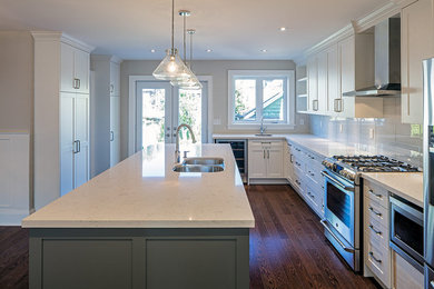 Mid-sized elegant l-shaped medium tone wood floor eat-in kitchen photo in Toronto with an undermount sink, shaker cabinets, white cabinets, quartz countertops, green backsplash, glass tile backsplash, stainless steel appliances and an island
