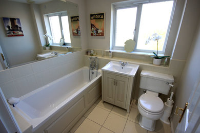 Photo of a mid-sized traditional kids bathroom in Other with shaker cabinets, beige cabinets, an alcove tub, a two-piece toilet, beige tile, ceramic tile, beige walls, ceramic floors, a drop-in sink and beige floor.