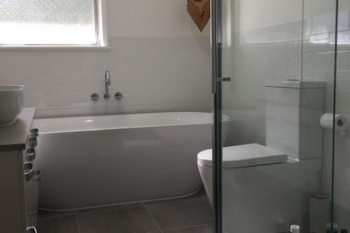 Design ideas for a mid-sized contemporary bathroom in Melbourne with flat-panel cabinets, white cabinets, a freestanding tub, a corner shower, a two-piece toilet, white tile, subway tile, white walls, ceramic floors, a vessel sink, granite benchtops, grey floor and a hinged shower door.