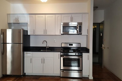 Example of a small transitional single-wall medium tone wood floor and brown floor enclosed kitchen design in New York with an undermount sink, shaker cabinets, white cabinets, solid surface countertops, stainless steel appliances, no island and black countertops