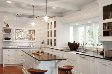 Example of a transitional medium tone wood floor kitchen design in Cleveland with a farmhouse sink, white cabinets, white backsplash, subway tile backsplash, paneled appliances, an island, recessed-panel cabinets and granite countertops