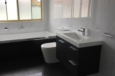 Photo of a mid-sized contemporary master bathroom in Sydney with dark wood cabinets, a drop-in tub, a corner shower, a one-piece toilet, white tile, ceramic tile, white walls, porcelain floors, black floor and a hinged shower door.