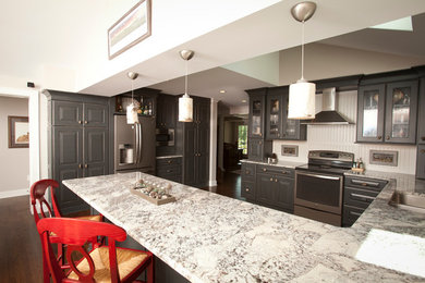 Inspiration for a large transitional u-shaped dark wood floor and brown floor kitchen remodel in Cincinnati with a double-bowl sink, glass-front cabinets, dark wood cabinets, granite countertops, white backsplash, stainless steel appliances, a peninsula and gray countertops